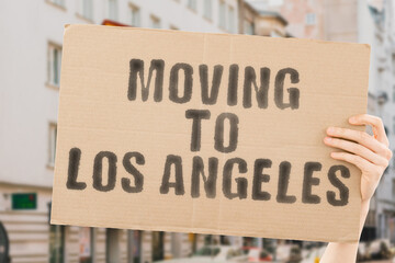 The phrase " Moving to Los Angeles " drawn on a carton banner in men's hand. Human holds a cardboard with an inscription. Big city. Urban. Opportunity. Immigration