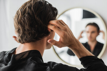 Young man touching hair near blurred mirror in bathroom