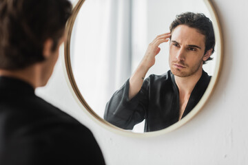 Blurred man in silk robe touching hair while looking at mirror in bathroom