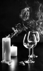 extinguished candles and glass goblets on a black background. smoke from candles and graceful...