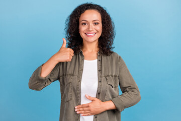 Portrait of attractive cheerful wavy-haired girl touching belly showing thumbup isolated over...