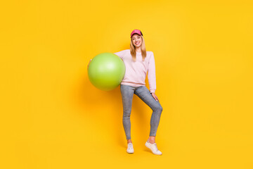 Photo of cute charming young lady wear pink sweater headwear smiling holding fit ball isolated yellow color background