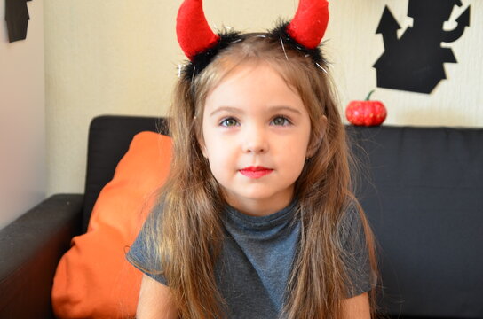 The girl makes funny faces, plays with a cloak for halloween. trick or treat. A girl in a devil costume, with horns on her head, a spider web make-up on her face. merry and happy halloween. Joyful