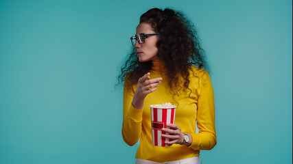 curly young woman holding popcorn bucket isolated on turquoise