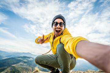 Young hiker man taking selfie portrait on the top of mountain - Happy guy smiling at camera -...