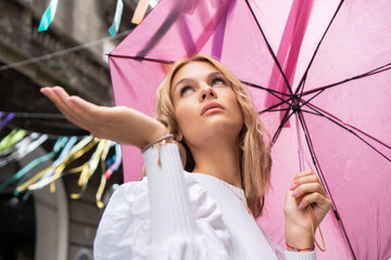 A beautiful blond teenage girl with a pink umbrella is joining the street carnival.