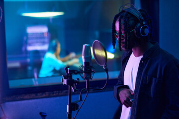 African young singer in headphones singing to microphone during recording of his song in the studio