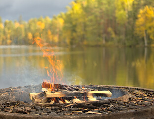 Campfire in front and colorful forest with reflections on water in background