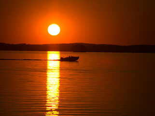 A boat crossing sun bridge on a lake during sunset in late evening