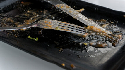 Dirty plate with metal fork and knife. leftover food on black plate with fork and knife