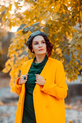 Beautiful woman walks outdoors in autumn. She is wearing a yellow coat and a green dress. Young woman enjoying the autumn weather. Autumn content.