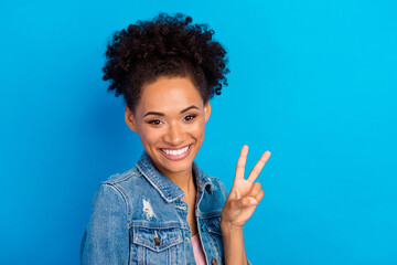 Photo of cheerful positive happy afro american woman show v-sign good mood isolated on blue color background