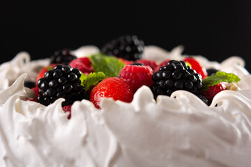 Delicious Pavlova cake with meringue topped and fresh berries on black background