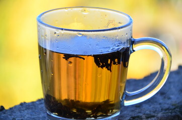 hot tea on a background of autumn foliage, boiling water is poured, leaves of tea leaves float. A Cup of hot tea with steam in a woman's hands. holding a Cup of hot tea outside. Steam from a Cup