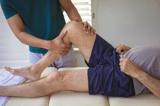 Biracial male physiotherapist treating leg of senior male patient at clinic