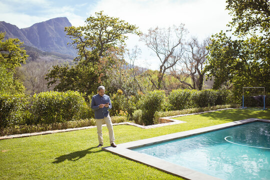 Senior biracial man using smartphone at swimming pool in garden
