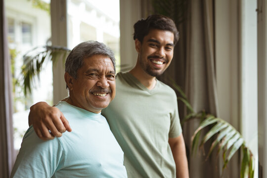 Portrait of smiling biracial adult son and senior father looking at camera and embracing