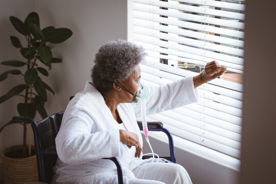 African american senior woman sitting on wheelchair with oxygen mask and looking through window