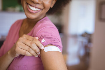 Smiling african american woman showing bandage on arm after covid vaccination