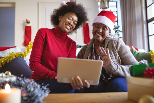 Happy african american senior woman and adult daughter in santa hats making christmas video call