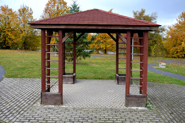 Pergola, garden gazebo completely empty after completion in autumn. public rest place in the park. The pergola has a square floor plan. lawn, shingle roof