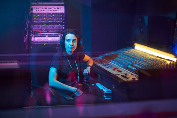 Young music producer in headphones sitting at the music keyboard and writing songs in the studio