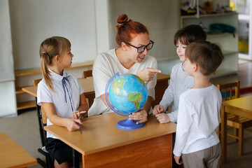 teacher and children in class are looking at globe, teacher helps explain the lesson to the...