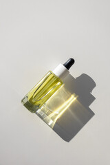 Facial yellow oil serum glass bottle with pipette on white background with bright sunbeam...