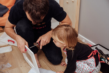 Little cute daughter helps her father fixing wooden furniture, using screwdriver, view from the top. 