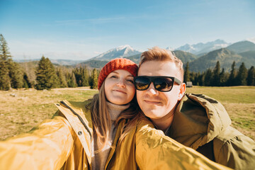 Couple making selfie photo high in the snow mountains enjoying the view. Freedom, happiness, travel and vacations concept, outdoor activities, she wearing in red hat and he a green jacket