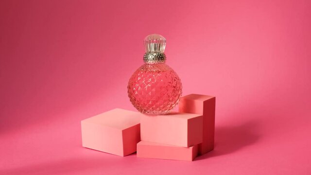 geometric podiums and pink crystal perfume spray bottle with silver cap, hard shadows, sunlight, reflexes and glare on pink background, palm leaf shadow