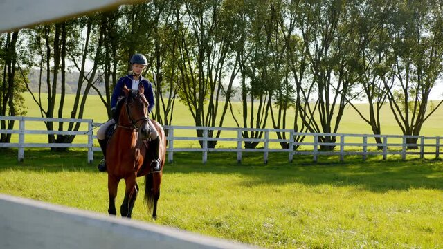 Full length view of the female jockey riding calmly on horseback at the meadow with fence. Horseback riding concept