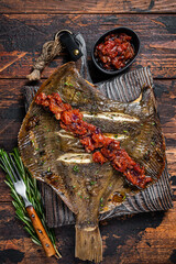 Grilled Flounder or plaice with  tomato sauce on wooden cutting board. Dark wooden background. Top view