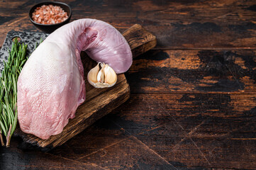 Uncooked Raw beef or veal tongue on butcher board with meat cleaver. Dark wooden background. Top...