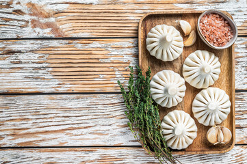 Frozen Raw dumplings Khinkali with beef and lamb meat on wooden tray with herbs. White wooden background. Top view. Copy space