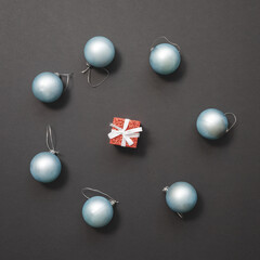 Light blue Christmas balls lie around a small red gift box against a dark background. New Year mockup