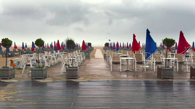Rainy day at the sandy beach of Deauville resort in Normandy, France, with its sunbeds and typical red and blue umbrellas.