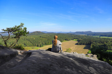 A woman is sitting on mountain Pfaffenstein with view at mountain Gohrischstein, Saxon Switzerland...