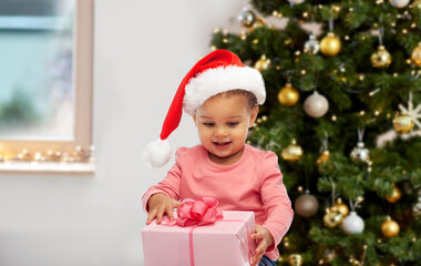 Fototapeta na wymiar childhood, winter holidays and people concept - happy smiling little baby girl with gift box over christmas tree background