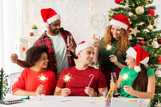 christmas, celebration and winter holidays concept - happy team in santa hats with sparklers and non-alcoholic champagne at corporate office party over christmas tree background - Powered by Adobe