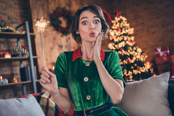 Photo of excited funny lady hand cheek open mouth hold bengal fire wear elf costume in decorated home indoors