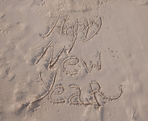 Inscription Happy New Year written in white sand of a beach. Celebrating the New Year in hot countries. New Year and travel content.