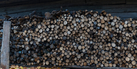 Neatly stacked big pile of chopped fire wood logs prepared for winter at vintage wooden barn wall. Texture for design.