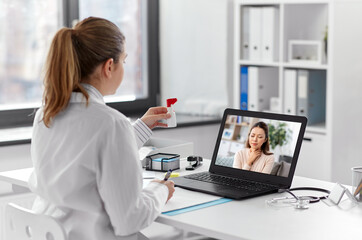 healthcare, technology and medicine concept - female doctor having video call with sick woman patient on laptop computer at hospital and showing oral spray
