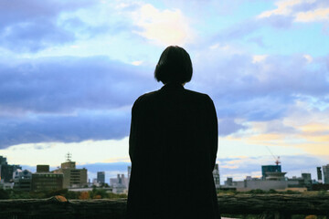 Fototapeta premium 夕方の空と街並みを眺める女性のシルエット