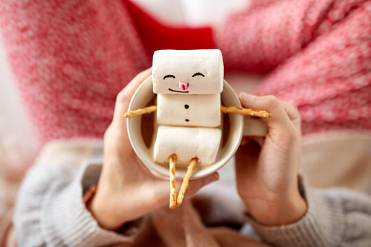 christmas, winter holidays and leisure concept - close up of hands holding mug with marshmallow snowman at home
