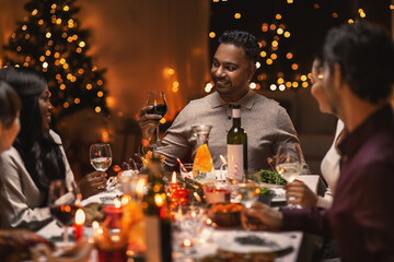 holidays, party and celebration concept - multiethnic group of happy friends having christmas dinner at home and drinking wine