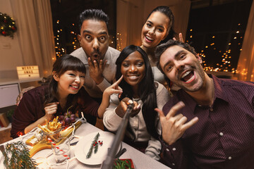 holidays, friendship and celebration concept - multiethnic group of happy friends having christmas dinner at home and taking selfie