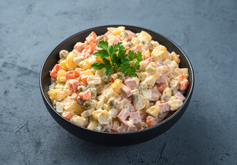 Olivier salad in a black bowl close-up on a graphite background. Side view, horizontal.