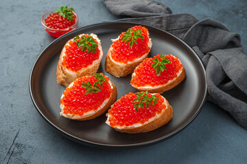 Sandwiches with red caviar, butter and parsley on a black plate on a dark background. Side view, close-up.